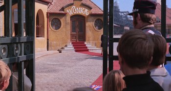 Movie still from “Willy Wonka & the Chocolate Factory” (1971), directed by Mel Stuart – A group of people standing in front of a building; Wide shot, Over the shoulder angle