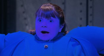 Movie still from “Willy Wonka & the Chocolate Factory” (1971), directed by Mel Stuart – A young girl in a blue jacket with a surprised look on her face; Medium shot, Over the shoulder angle