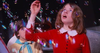 Movie still from “Willy Wonka & the Chocolate Factory” (1971), directed by Mel Stuart – A girl in a red dress and a boy in a yellow shirt are playing with bubbles; Medium shot, Low angle