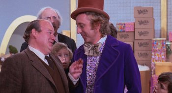 Movie still from “Willy Wonka & the Chocolate Factory” (1971), directed by Mel Stuart – A man wearing a purple jacket and a brown top hat; Medium shot, Over the shoulder angle