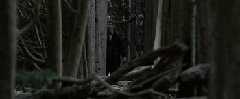 Movie still from “Winnie the Pooh: Blood and Honey” (2023), directed by Rhys Frake-Waterfield – A man walking through the woods near a pile of wood; Wide shot, Low angle