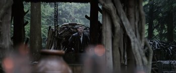 Movie still from “Winnie the Pooh: Blood and Honey” (2023), directed by Rhys Frake-Waterfield – A man standing in front of a pile of wood; Wide shot, Over the shoulder angle