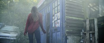Movie still from “Winnie the Pooh: Blood and Honey” (2023), directed by Rhys Frake-Waterfield – A woman walking in front of a blue door; Wide shot, Low angle