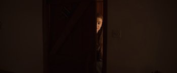 Movie still from “Winnie the Pooh: Blood and Honey” (2023), directed by Rhys Frake-Waterfield – A young girl peeks out from a door way; Medium shot, Over the shoulder angle