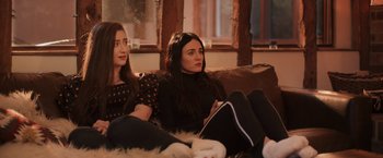 Movie still from “Winnie the Pooh: Blood and Honey” (2023), directed by Rhys Frake-Waterfield – Two young women sitting on a couch in a living room; Medium shot, Over the shoulder angle