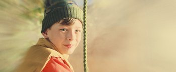 Movie still from “Winnie the Pooh: Blood and Honey” (2023), directed by Rhys Frake-Waterfield – A young boy wearing a green hat on a swing; Close Up shot, Low angle
