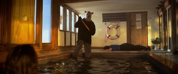 Movie still from “Winnie the Pooh: Blood and Honey” (2023), directed by Rhys Frake-Waterfield – A man with a cat mask holding a stick in a room; Wide shot, Low angle