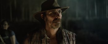 Movie still from “Winnie the Pooh: Blood and Honey” (2023), directed by Rhys Frake-Waterfield – A man wearing a hat and a plaid shirt looking to his left; Close Up shot, Low angle