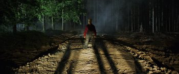 Movie still from “Winnie the Pooh: Blood and Honey” (2023), directed by Rhys Frake-Waterfield – A man in a red shirt is standing on a dirt road; Wide shot, Low angle