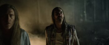 Movie still from “Winnie the Pooh: Blood and Honey” (2023), directed by Rhys Frake-Waterfield – A man with long black hair and a plaid shirt; Medium shot, Low angle