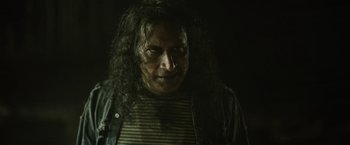 Movie still from “Winnie the Pooh: Blood and Honey” (2023), directed by Rhys Frake-Waterfield – A man with long black hair and a striped t - shirt; Close Up shot, Low angle