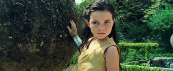Movie still from “Wonder Woman” (2017), directed by Patty Jenkins – A young girl in a yellow dress leaning against a tree; Close Up shot, Low angle