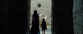 Movie still from “Wonder Woman” (2017), directed by Patty Jenkins – A woman and a child walking through a doorway; Wide shot, Low angle