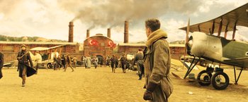 Movie still from “Wonder Woman” (2017), directed by Patty Jenkins – A man standing in front of a group of people in front of a factory; Wide shot, Low angle