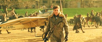 Movie still from “Wonder Woman” (2017), directed by Patty Jenkins – A man in a coat and gloves holding a camera in front of an airplane; Medium shot, Over the shoulder angle