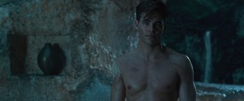 Movie still from “Wonder Woman” (2017), directed by Patty Jenkins – A shirtless man with no shirt in front of a rock wall; Medium shot, Low angle