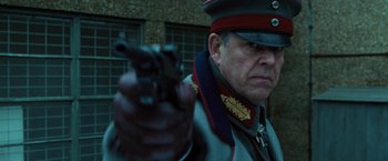 Movie still from “Wonder Woman” (2017), directed by Patty Jenkins – A man in military uniform holding a gun in front of a brick building; Close Up shot, Low angle