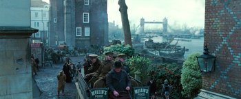 Movie still from “Wonder Woman” (2017), directed by Patty Jenkins – A group of men riding on the back of a horse drawn carriage down a street; Extreme Wide shot, High angle