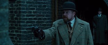 Movie still from “Wonder Woman” (2017), directed by Patty Jenkins – A man in a hat and a coat holding a gun; Medium shot, Over the shoulder angle