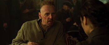 Movie still from “Wonder Woman” (2017), directed by Patty Jenkins – An old man with a goatee is holding a drink; Close Up shot, Over the shoulder angle