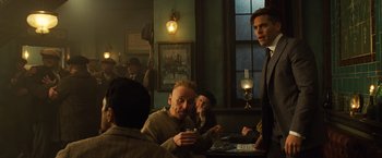 Movie still from “Wonder Woman” (2017), directed by Patty Jenkins – A group of men sitting at a table in front of a window; Medium shot, Over the shoulder angle