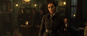 Movie still from “Wonder Woman” (2017), directed by Patty Jenkins – A woman in a coat and hat standing in a room; Medium shot, Over the shoulder angle