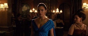 Movie still from “Wonder Woman” (2017), directed by Patty Jenkins – Gal gadot in a blue dress in front of a group of people; Medium shot, Over the shoulder angle