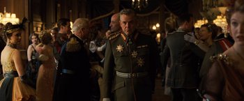 Movie still from “Wonder Woman” (2017), directed by Patty Jenkins – An older man in a military uniform standing in front of a group of people; Medium shot, Over the shoulder angle