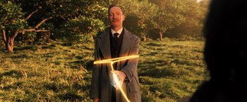 Movie still from “Wonder Woman” (2017), directed by Patty Jenkins – A man in a suit and tie holding a light saber; Medium shot, Over the shoulder angle