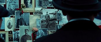 Movie still from “Wonder Woman” (2017), directed by Patty Jenkins – A man in a suit and hat looking at a wall of old photos; Close Up shot, Over the shoulder angle