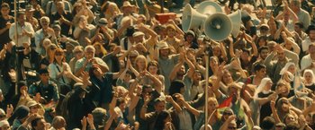 Movie still from “World War Z” (2013), directed by Marc Forster – A crowd of people standing in a stadium with megaphones; Wide shot, High angle