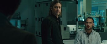 Movie still from “World War Z” (2013), directed by Marc Forster – A man standing in front of a camera in a room; Medium shot, Over the shoulder angle
