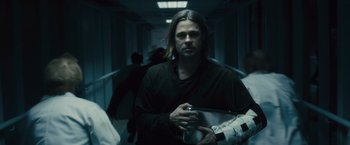 Movie still from “World War Z” (2013), directed by Marc Forster – A man with long blonde hair is walking down a hallway; Medium shot, Over the shoulder angle