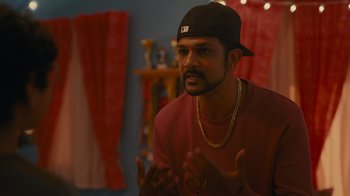 Movie still from “World's Best” (2023), directed by Roshan Sethi – A man wearing a black hat talking to someone; Medium shot, Over the shoulder angle