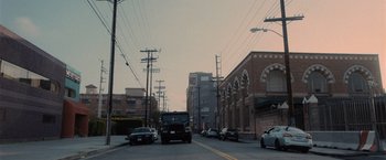 Movie still from “Wrath of Man” (2021), directed by Guy Ritchie – Cars driving down a street near a building; Extreme Wide shot, Low angle