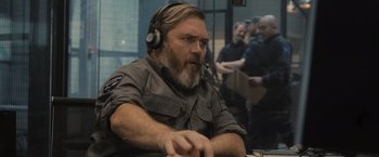 Movie still from “Wrath of Man” (2021), directed by Guy Ritchie – A man with a beard wearing a headset; Medium shot, Over the shoulder angle