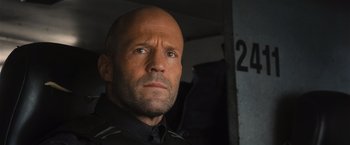 Movie still from “Wrath of Man” (2021), directed by Guy Ritchie – A man with a shaved head and a black shirt; Close Up shot, Low angle