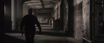 Movie still from “Wrath of Man” (2021), directed by Guy Ritchie – A person walking in a dark room with a bunch of lights; Wide shot, Low angle