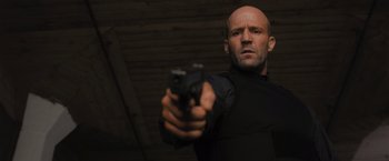 Movie still from “Wrath of Man” (2021), directed by Guy Ritchie – A bald man in black is holding a gun; Close Up shot, Low angle
