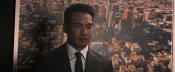 Movie still from “Wrath of Man” (2021), directed by Guy Ritchie – A man wearing a suit and tie standing in front of a city skyline; Close Up shot, Over the shoulder angle