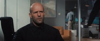 Movie still from “Wrath of Man” (2021), directed by Guy Ritchie – A man with a bald head in a black shirt; Close Up shot, Over the shoulder angle