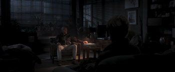 Movie still from “Wrath of Man” (2021), directed by Guy Ritchie – An older man sitting in a chair in a dark room; Wide shot, High angle