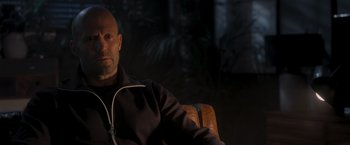 Movie still from “Wrath of Man” (2021), directed by Guy Ritchie – A bald man sitting in a leather chair; Close Up shot, Over the shoulder angle