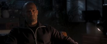 Movie still from “Wrath of Man” (2021), directed by Guy Ritchie – A bald man wearing headphones sitting in a chair; Close Up shot, Over the shoulder angle