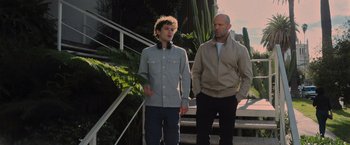 Movie still from “Wrath of Man” (2021), directed by Guy Ritchie – A man and a woman standing next to each other on steps; Medium shot, Over the shoulder angle