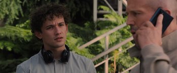 Movie still from “Wrath of Man” (2021), directed by Guy Ritchie – A young man with headphones standing in front of some trees; Close Up shot, Over the shoulder angle