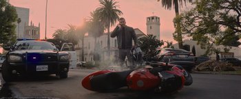 Movie still from “Wrath of Man” (2021), directed by Guy Ritchie – A man standing next to a motorcycle on the side of the road; Wide shot, Low angle
