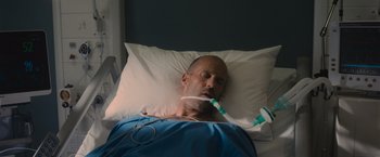 Movie still from “Wrath of Man” (2021), directed by Guy Ritchie – A man laying in a hospital bed with an oxygen mask on; Close Up shot, Overhead angle