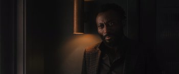 Movie still from “Wrath of Man” (2021), directed by Guy Ritchie – A man with a beard and a jacket on; Close Up shot, Over the shoulder angle