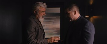 Movie still from “Wrath of Man” (2021), directed by Guy Ritchie – Two men standing next to each other in front of a window; Medium shot, Over the shoulder angle